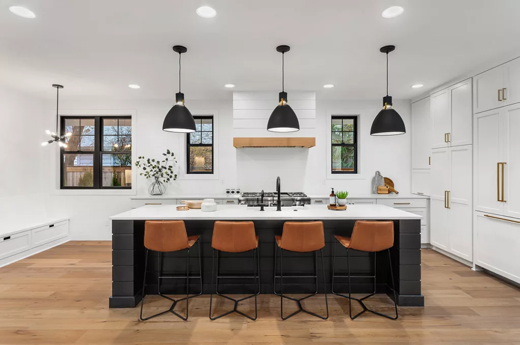 A modern kitchen with white walls, wooden floors, and black lighting fixtures hanging from the ceiling.