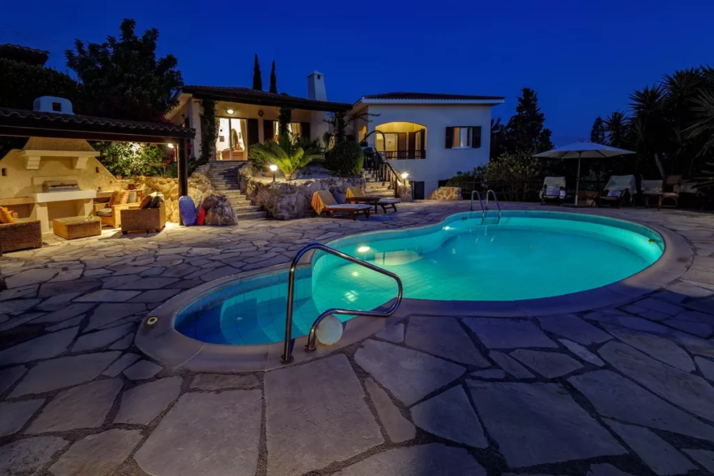 A backyard swimming pool at dusk, illuminated by swimming pool lighting