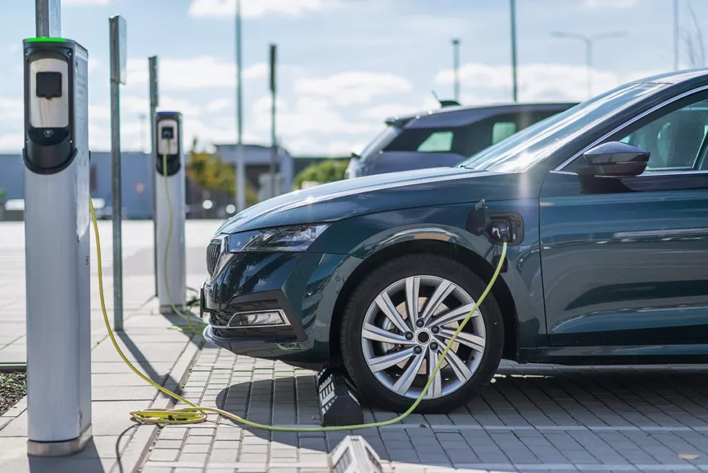 A dark gray electric vehicle in a parking lot, charging at an EV charging station.