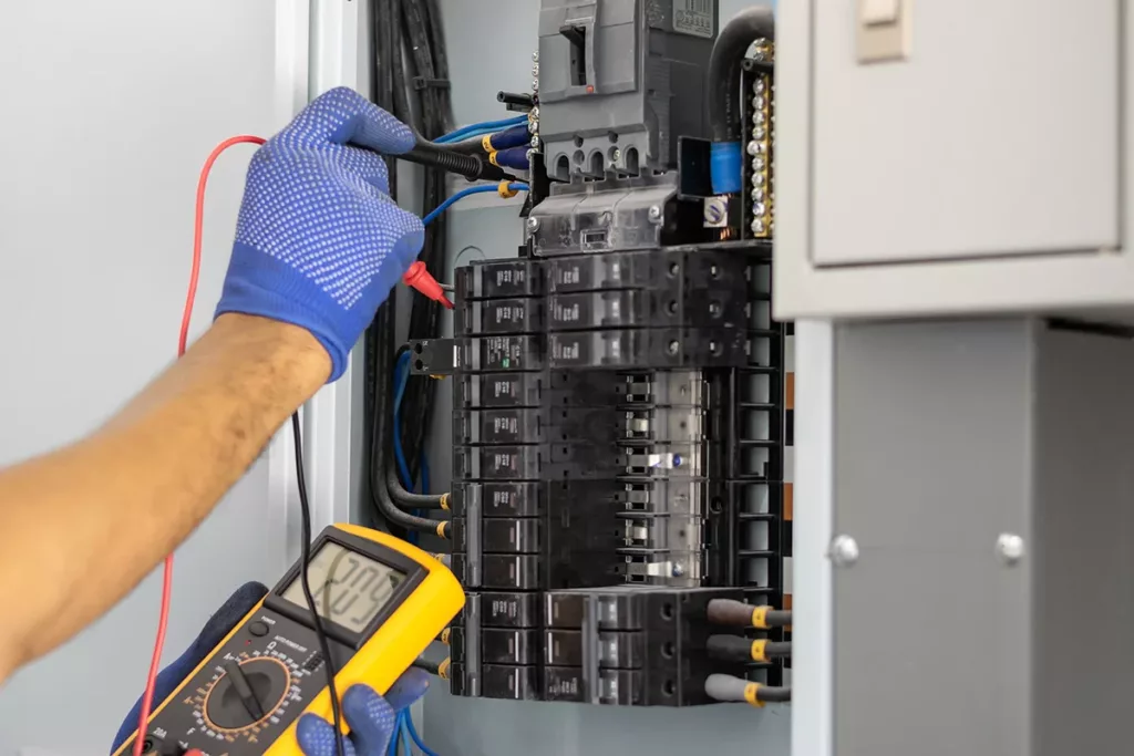 A commercial electrician wearing a blue glove inspects a circuit breaker