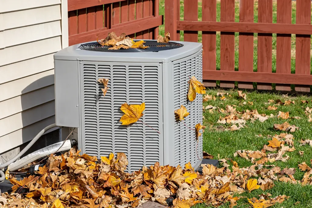 An air conditioning unit outside, surrounded by autumn leaves