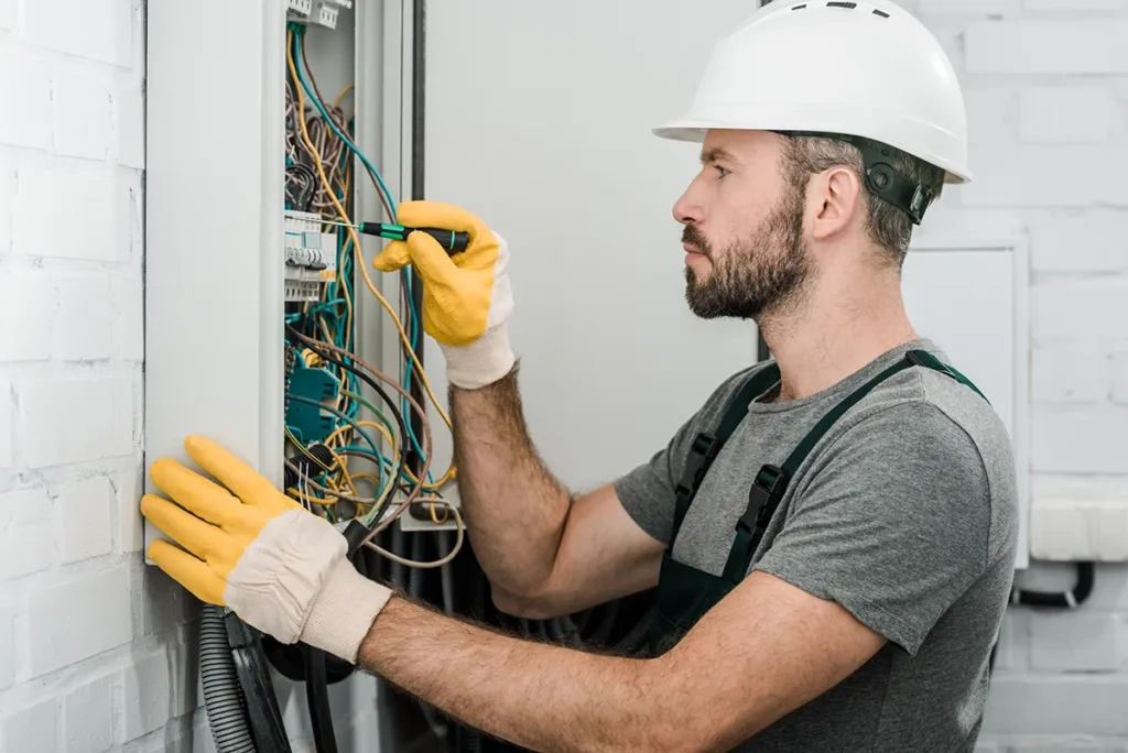 A residential electrician wearing a white hard hat, fixing electrical wiring