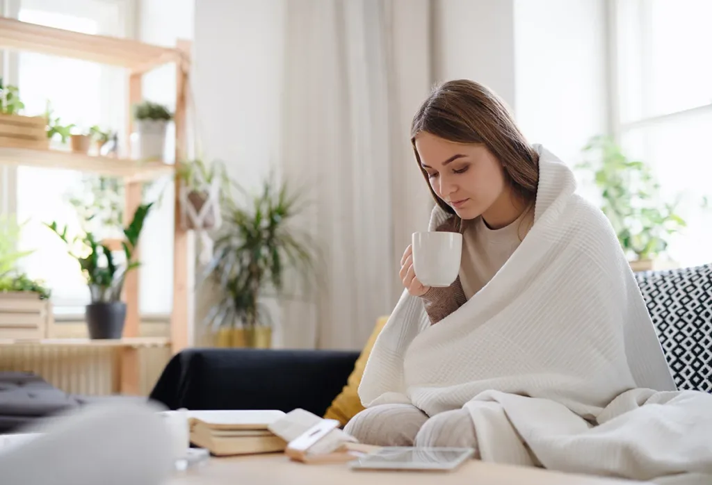 A young girl sipping coffee with a blanket to stay warm during winter and lower electric bill